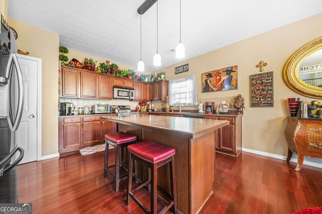 kitchen featuring tasteful backsplash, stainless steel appliances, brown cabinetry, and dark wood-style flooring