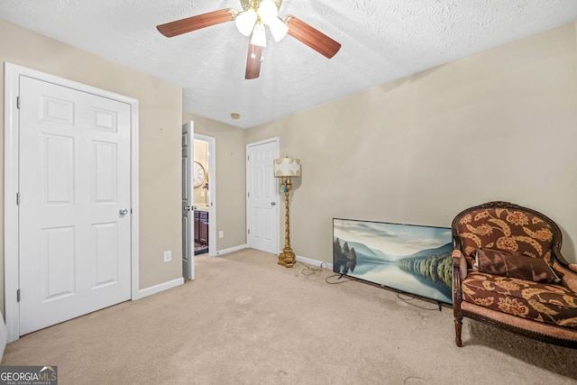 living area with a ceiling fan, light colored carpet, baseboards, and a textured ceiling