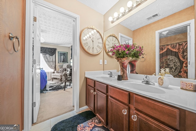 ensuite bathroom featuring tile patterned flooring, visible vents, double vanity, a textured ceiling, and a sink