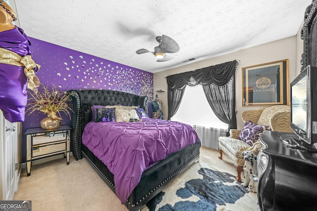 carpeted bedroom with wallpapered walls, a ceiling fan, visible vents, and a textured ceiling