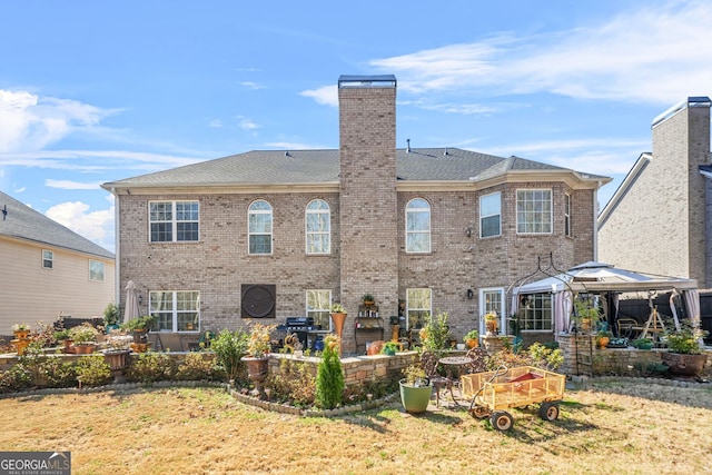 rear view of house with a gazebo, brick siding, a chimney, and a patio area