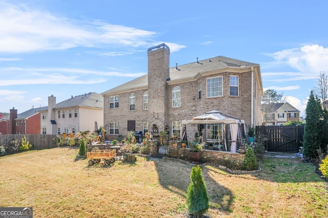 rear view of house featuring a yard, a chimney, brick siding, and a fenced backyard