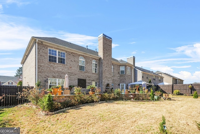 back of house featuring brick siding, a chimney, a yard, a fenced backyard, and a patio