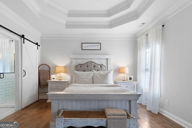 bedroom with a barn door, a tray ceiling, visible vents, wood-type flooring, and crown molding
