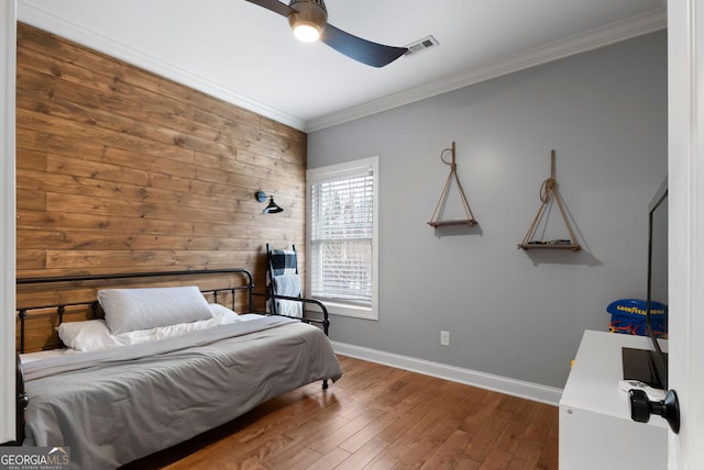bedroom featuring wood finished floors, wooden walls, baseboards, ornamental molding, and visible vents