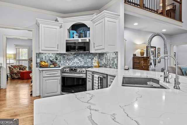 kitchen with light wood finished floors, light stone counters, stainless steel appliances, white cabinetry, and a sink