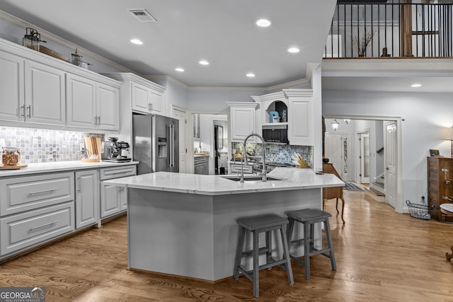 kitchen with light wood finished floors, ornamental molding, high end fridge, white cabinetry, and a sink