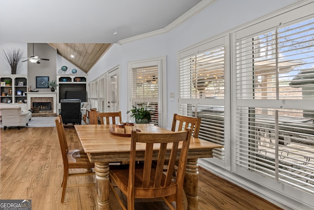 dining area with a fireplace, ornamental molding, ceiling fan, vaulted ceiling, and light wood-type flooring