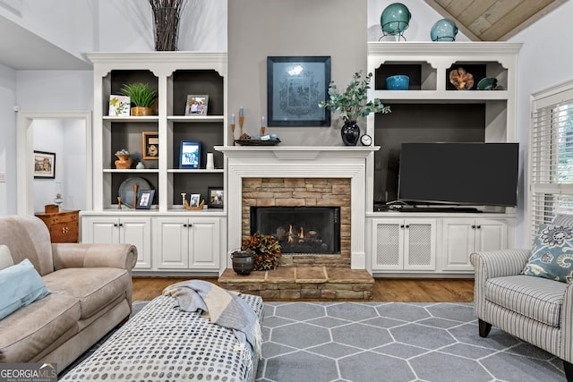 living room featuring built in shelves, a fireplace, lofted ceiling, and wood finished floors