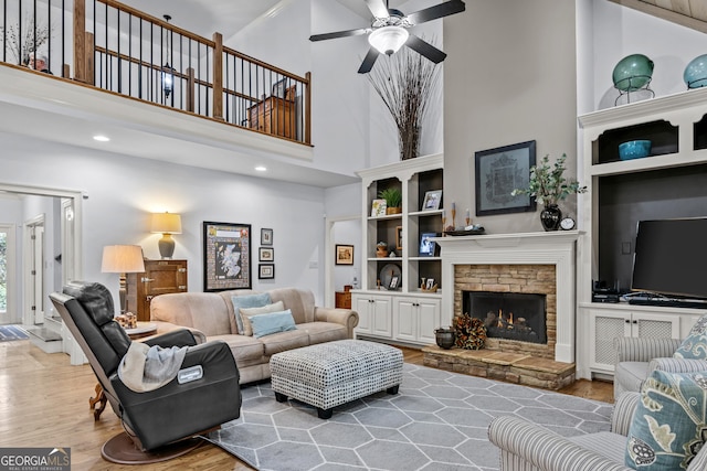 living room featuring ceiling fan, wood finished floors, recessed lighting, a fireplace, and a towering ceiling