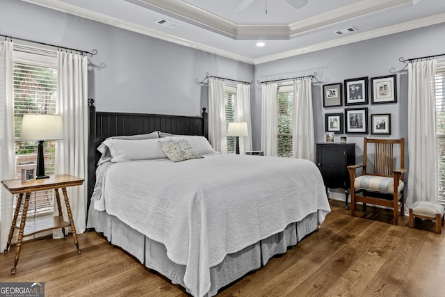 bedroom featuring visible vents, crown molding, a raised ceiling, and wood finished floors