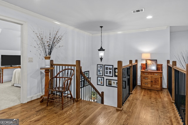 hall with wood finished floors, visible vents, recessed lighting, crown molding, and an upstairs landing