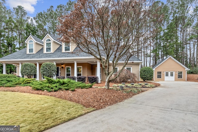 cape cod home featuring brick siding, covered porch, driveway, and a front lawn