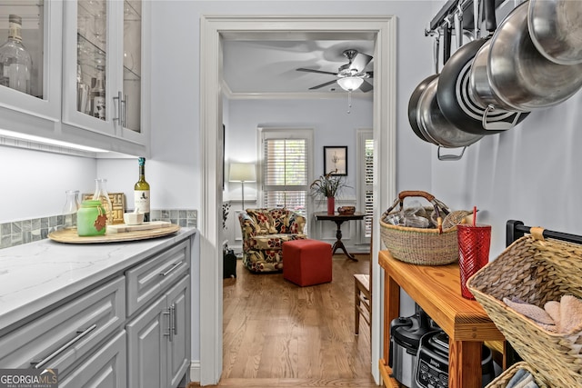 kitchen with gray cabinetry, glass insert cabinets, light stone counters, wood finished floors, and a ceiling fan