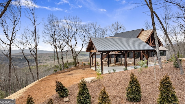 view of side of home featuring stone siding, a mountain view, metal roof, and a patio