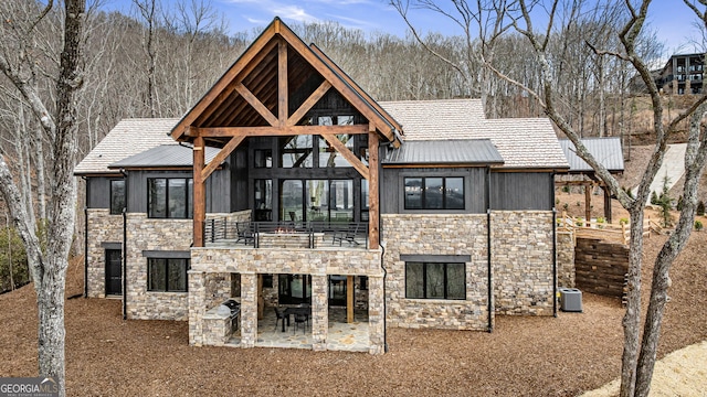 back of house with a balcony, stone siding, central air condition unit, a patio area, and board and batten siding