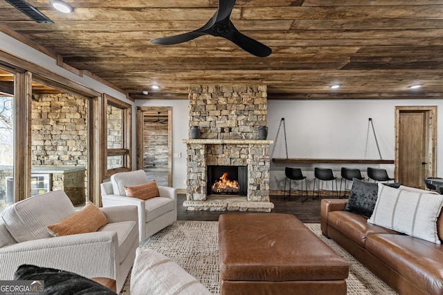 living room featuring visible vents, wood finished floors, a stone fireplace, wooden ceiling, and ceiling fan