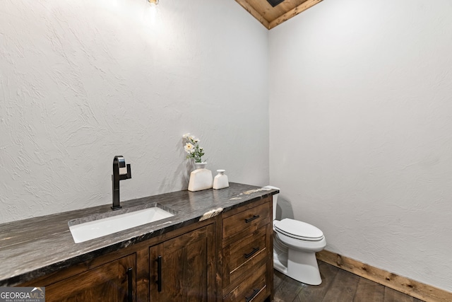 bathroom featuring toilet, wood finished floors, baseboards, vanity, and a textured wall