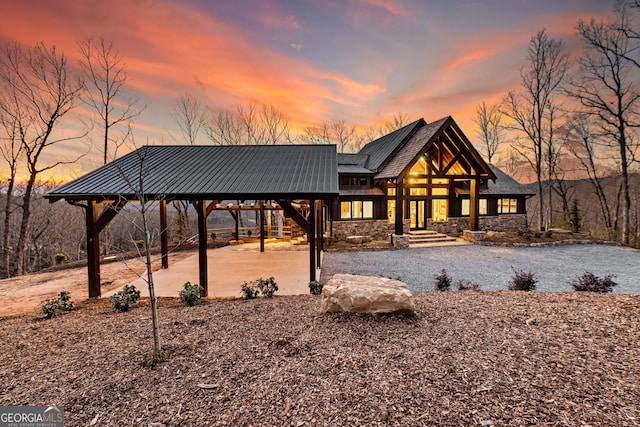 view of front of house featuring stone siding, driveway, and metal roof