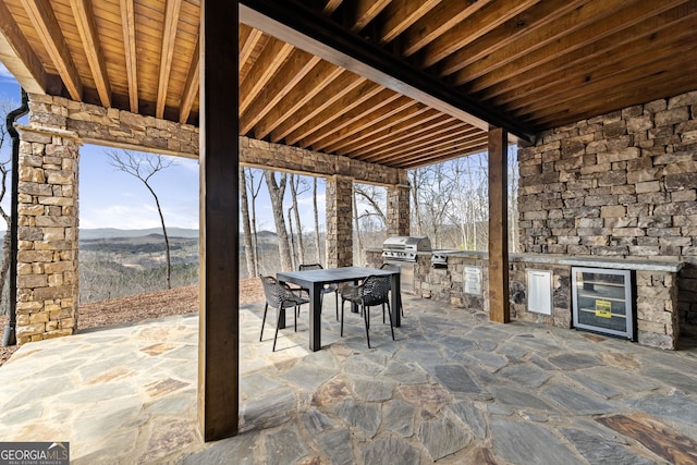 view of patio / terrace with outdoor dining space, beverage cooler, exterior kitchen, area for grilling, and a mountain view