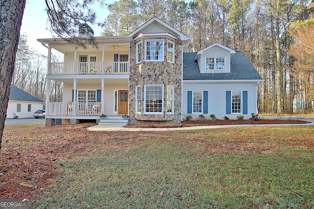 traditional-style house featuring a balcony, a porch, stucco siding, a front lawn, and stone siding