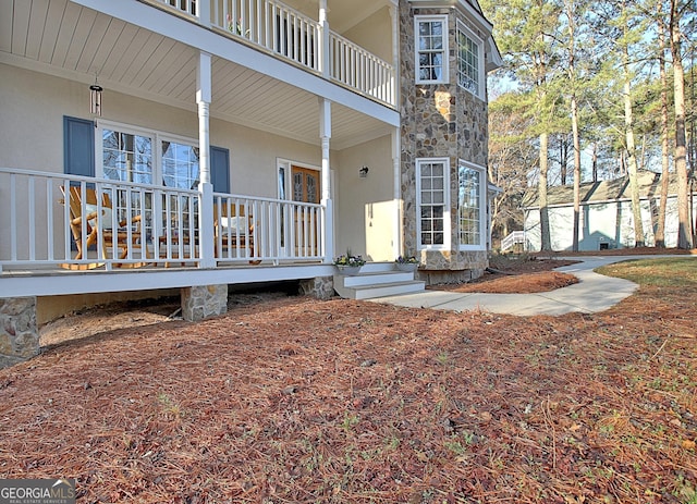 doorway to property with covered porch, stone siding, and stucco siding