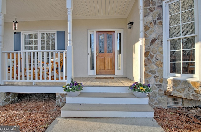 doorway to property featuring a porch, visible vents, stone siding, and stucco siding