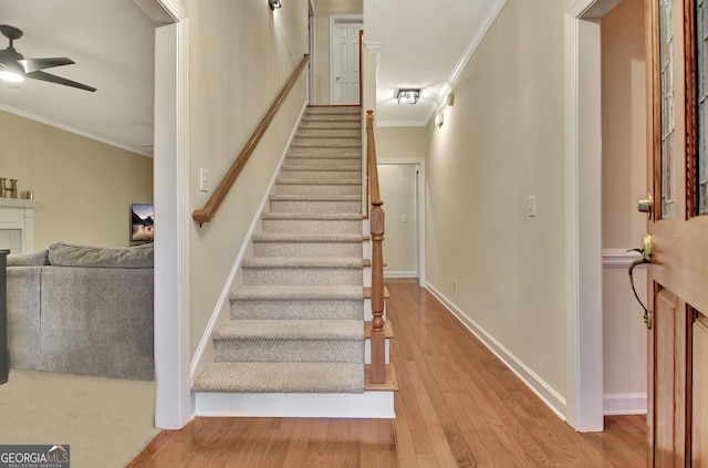 stairs featuring baseboards, wood finished floors, ceiling fan, and crown molding