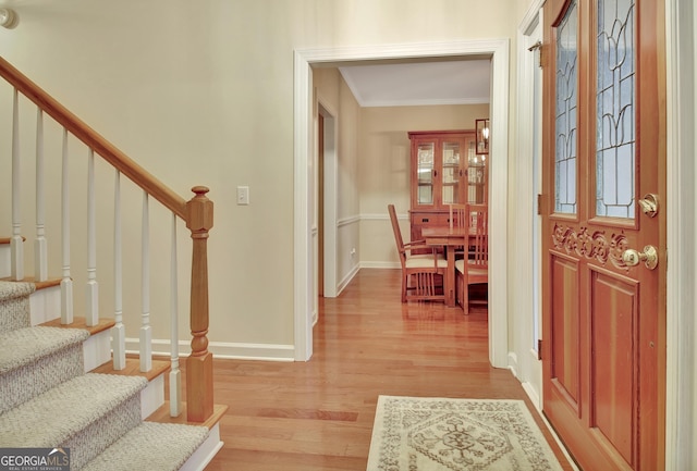 entrance foyer with light wood finished floors, crown molding, stairs, and baseboards