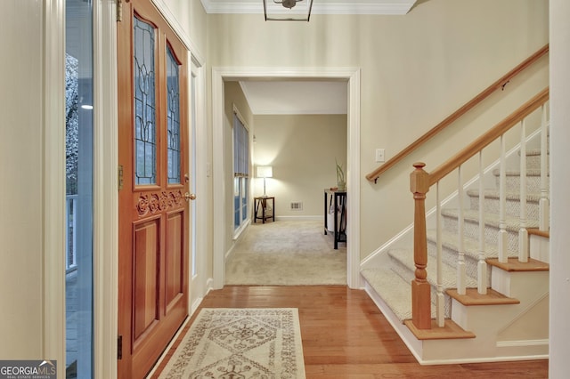 foyer entrance featuring visible vents, ornamental molding, wood finished floors, stairway, and baseboards