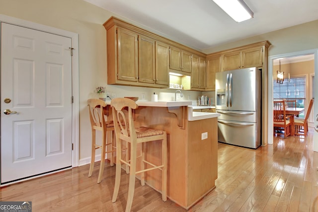 kitchen featuring light countertops, a kitchen breakfast bar, a peninsula, light wood-style floors, and stainless steel refrigerator with ice dispenser