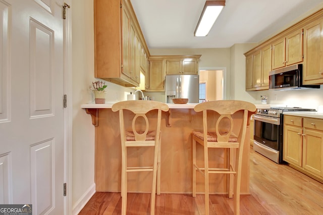 kitchen with a breakfast bar, a sink, light wood-style floors, appliances with stainless steel finishes, and light countertops