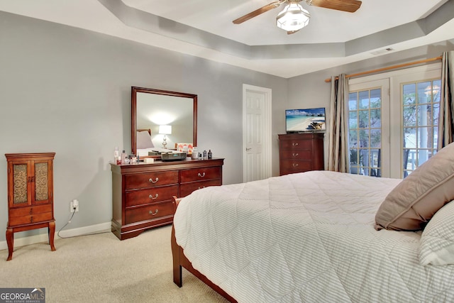 bedroom with visible vents, light carpet, a tray ceiling, baseboards, and ceiling fan