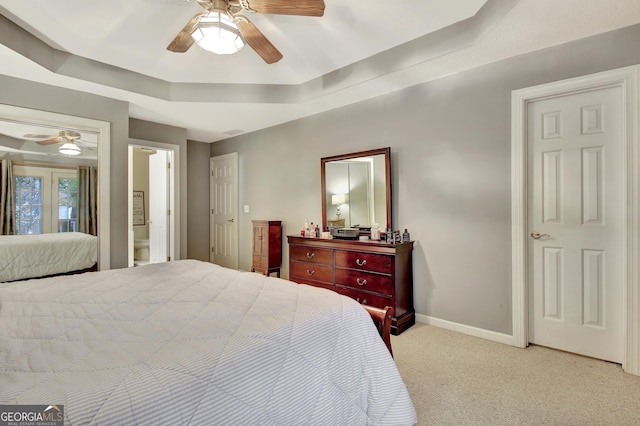 bedroom with a ceiling fan, baseboards, ensuite bath, a raised ceiling, and light colored carpet