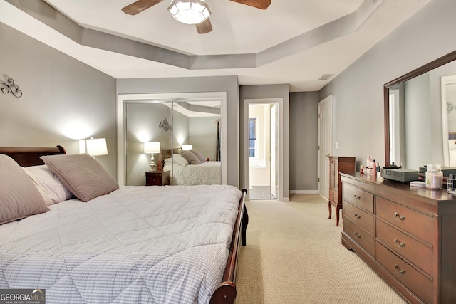 bedroom with light carpet, a raised ceiling, a closet, baseboards, and ceiling fan