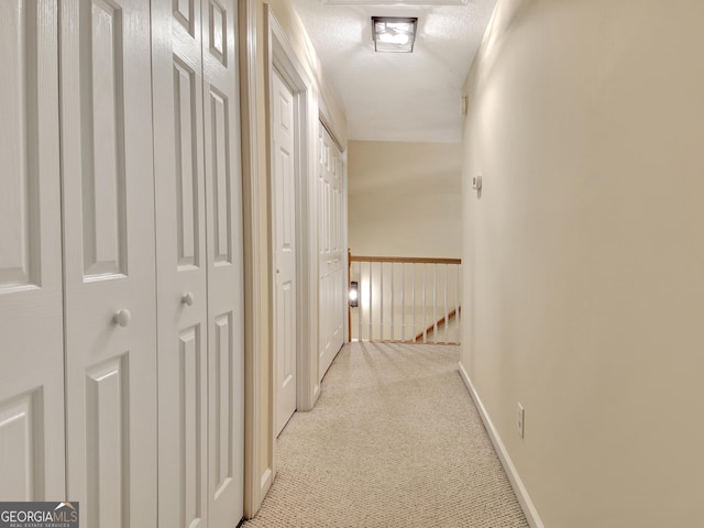 hallway featuring baseboards, an upstairs landing, a textured ceiling, and carpet floors