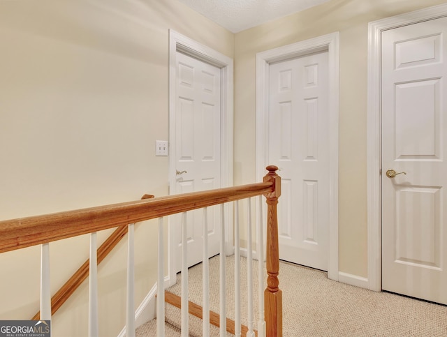 hall featuring baseboards, an upstairs landing, and light colored carpet