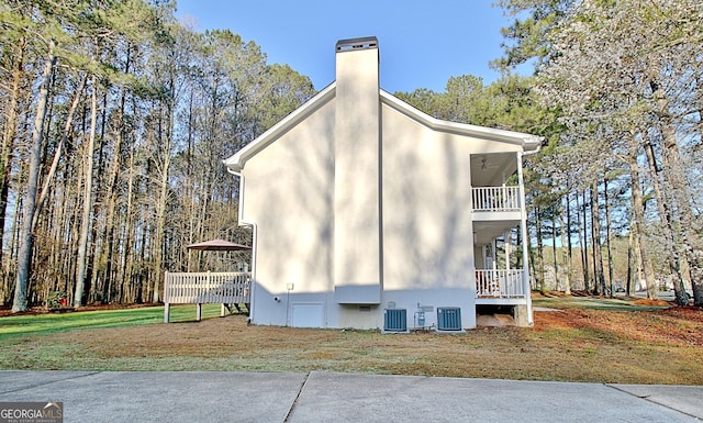 view of home's exterior featuring a balcony, a chimney, a lawn, and central AC