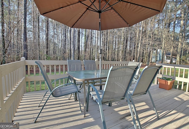 deck with a forest view and outdoor dining area