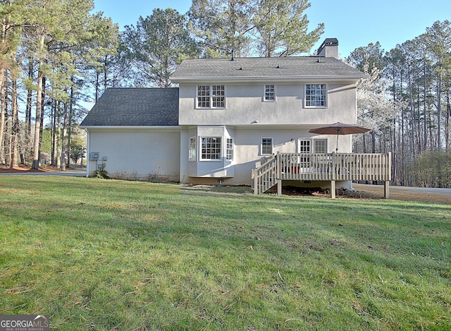 back of house with stucco siding, a lawn, a deck, roof with shingles, and a chimney