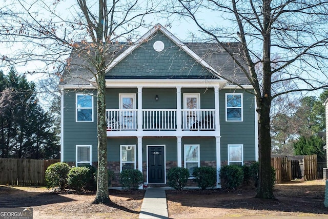 view of front of home featuring stone siding, a porch, fence, a shingled roof, and a balcony