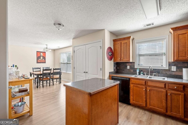 kitchen with light wood finished floors, a kitchen island, black dishwasher, and a sink