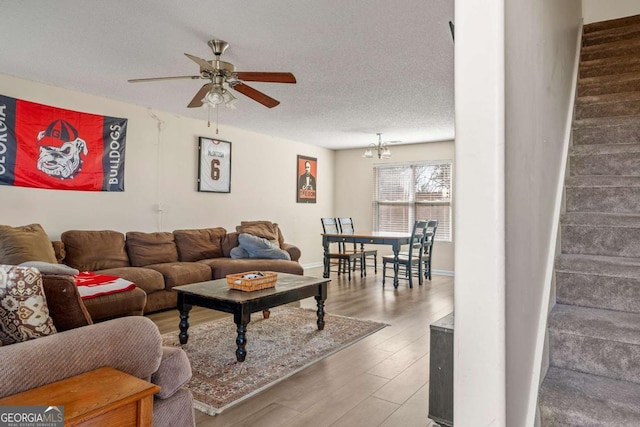 living area featuring wood finished floors, a ceiling fan, baseboards, stairs, and a textured ceiling