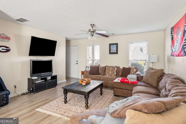 living area featuring a ceiling fan, wood finished floors, a healthy amount of sunlight, and visible vents