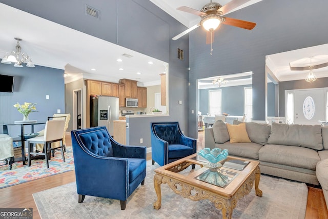 living room with light wood-type flooring, visible vents, crown molding, and ceiling fan with notable chandelier