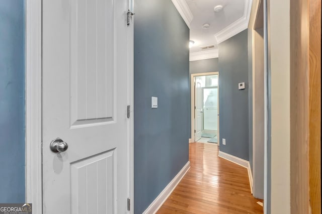 corridor featuring visible vents, baseboards, light wood-style floors, and ornamental molding