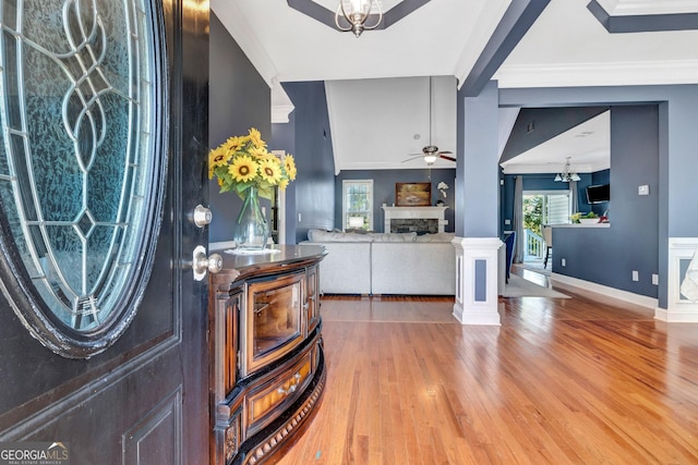 entrance foyer with wood finished floors, baseboards, a stone fireplace, crown molding, and ceiling fan with notable chandelier