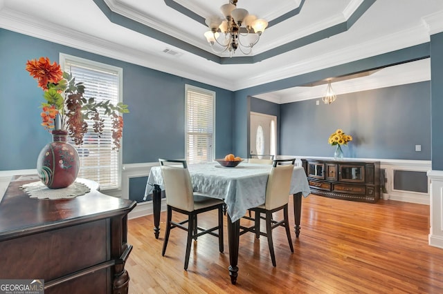 dining area featuring visible vents, a chandelier, a wainscoted wall, light wood-style flooring, and a raised ceiling