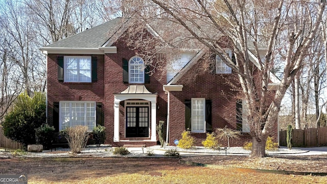 view of front of house featuring brick siding, roof with shingles, and fence