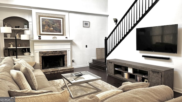 living area with a stone fireplace, stairway, wood finished floors, and baseboards